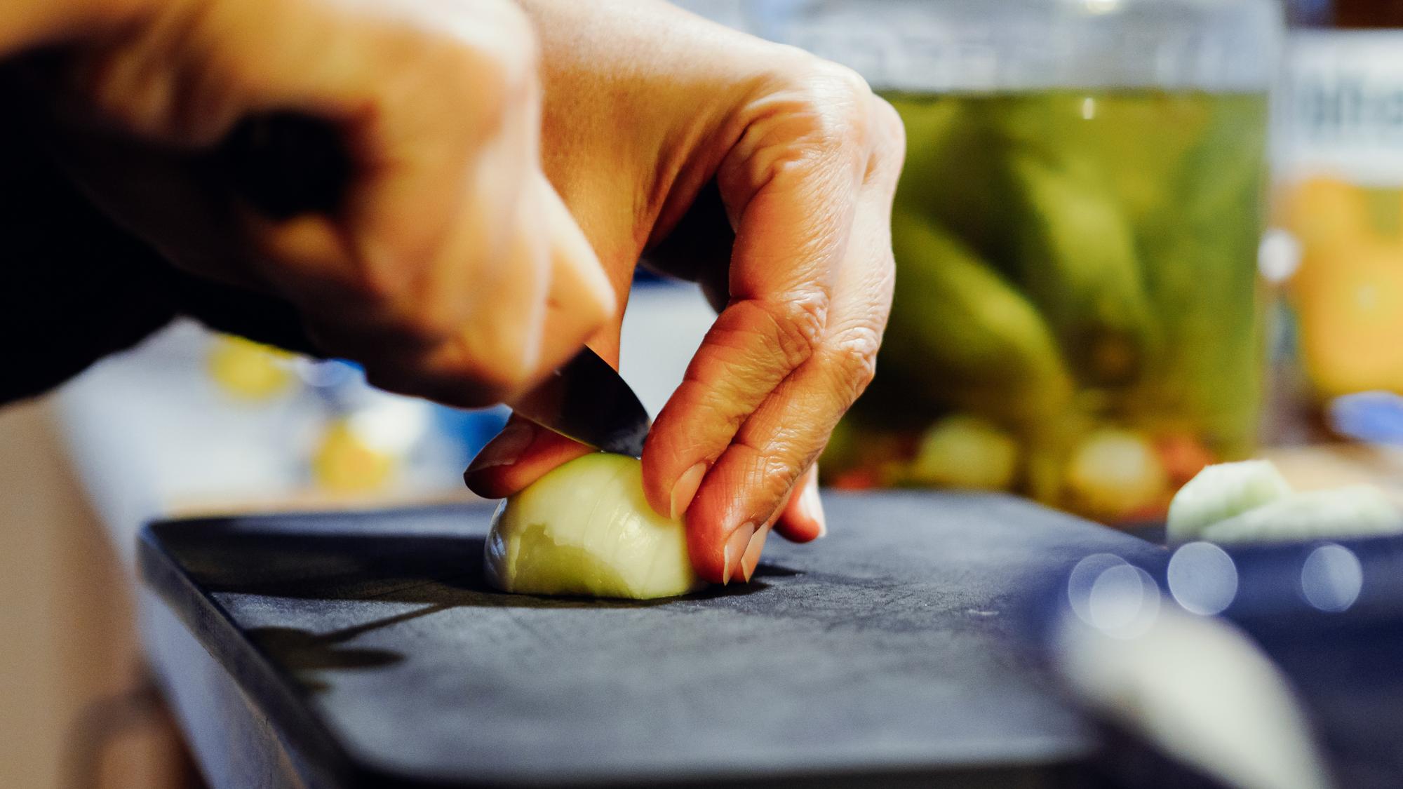 Mani di uno chef che affettano verdure con cura